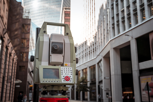 A surveying device set up on the street between buildings in central London.