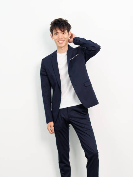 Portrait of handsome Chinese young man in dark blue leisure suit posing against white wall background. Hand on head and smiling at camera, looks confident. stock photo