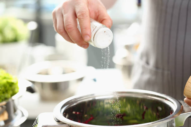 プロの料理人は塩セラーを保持し、キッチンの背景に対してスープに塩を追加します - salty water ストックフォトと画像