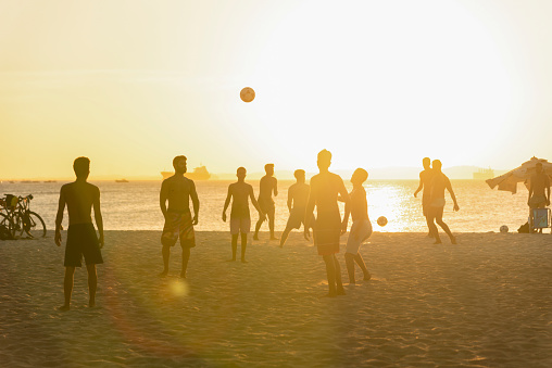 Salvador, Bahia, Brazil - December 23, 2020: Young people playing beach soccer during sunset at Ribeira beach in Salvador, Bahia, Brazil.