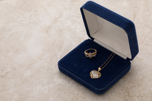 Mother's day Necklace in gold and white gold. Gold ring with Diamonds to match. Set inside a blue jewelry box on top of a white marble background.