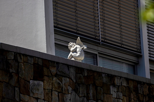 Little white statue of baby angel on stone wall, background with copy space, full frame horizontal composition