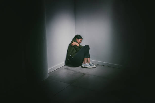 photo d’une jeune femme assise dans le coin d’une pièce sombre - claustrophobic photos et images de collection