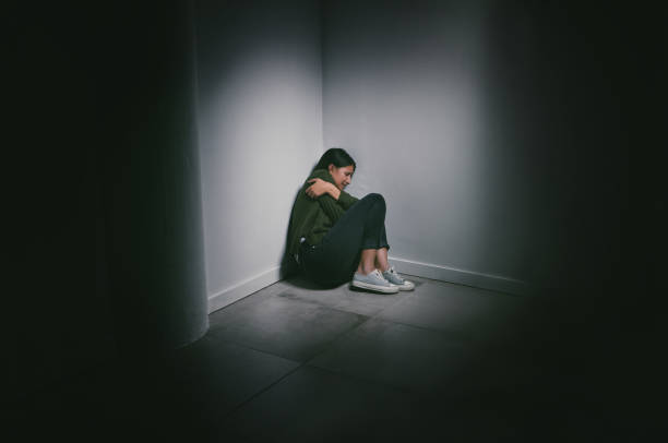 shot of a young woman sitting in the corner of a dark room - claustrophobic imagens e fotografias de stock