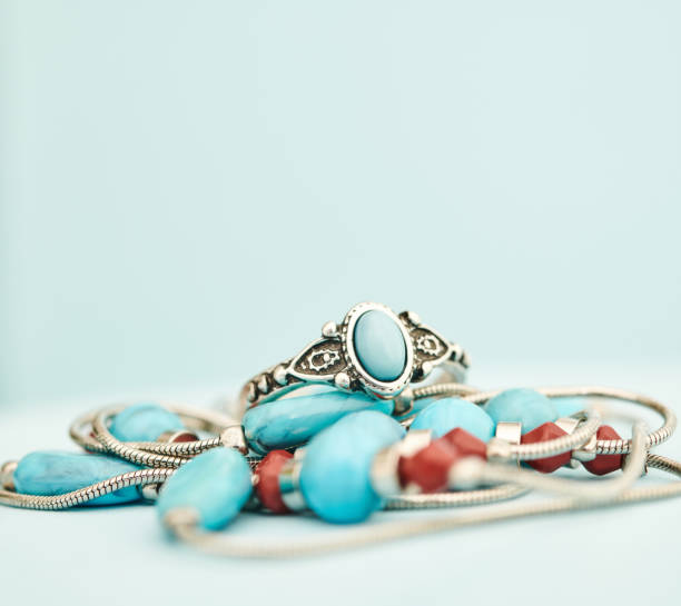 Turquoise and silver ring with beaded necklace in a bright studio setting with blue background. Western style jewelry