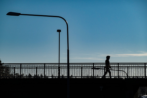Stockholm, Sweden Feb 20, 2022 A man in silhouette in the Flemingsberg suburb or district on a sunny winter day walks on a bridge.