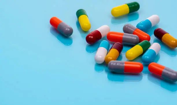 Photo of Antibiotic capsule pills on blue background. Prescription drugs. Colorful capsule pills. Antibiotic drug resistance concept. Pharmaceutical industry. Superbug problems. Medicament and pharmacology.