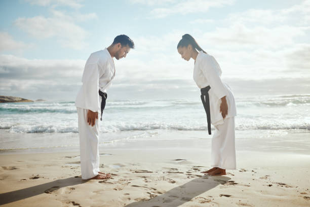 pełnometrażowe ujęcie dwóch młodych mistrzów sztuk walki ćwiczących karate na plaży - bowing zdjęcia i obrazy z banku zdjęć