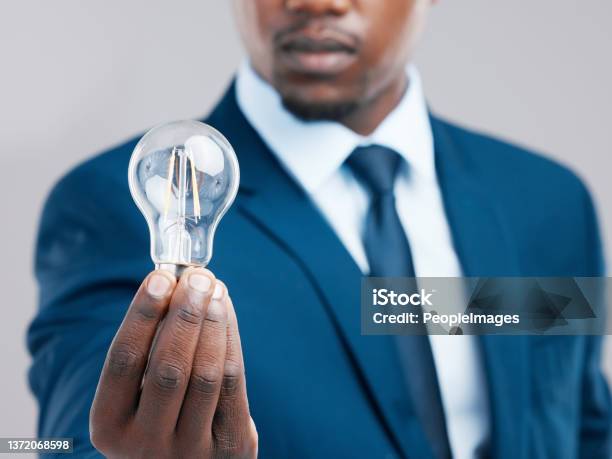 Studio Shot Of A Businessman Holding A Light Bulb Against A Grey Background Stock Photo - Download Image Now