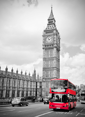 An iconic red London bus passing by Big Ben clocktower, color isolated black and white.