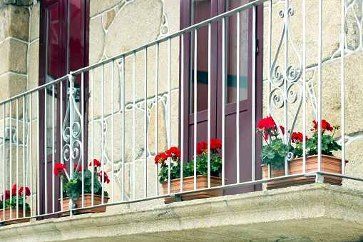 Cast iron balcony with flower pots, stone wall , red geraniums. Pontevedra province, Galicia, Spain.