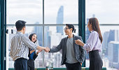 アジアのビジネスチームリーダーは、超高層ビルの景色を望む現代のオフィスワークプレイスで握手を交わすことによって、チームメイトの従業員の優れた業績チームのパフォーマンスを祝�