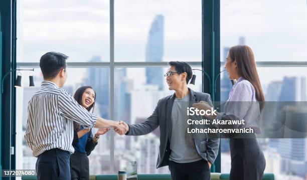 アジアのビジネスチームリーダーは、超高層ビルの景色を望む現代のオフィスワークプレイスで握手を交わすことによって、チームメイトの従業員の優れた業績チームのパフォーマンスを祝�