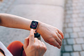 istock Over the shoulder view of young Asian sports woman checks her fitness statistics on smartwatch to monitor her training progress after working out in city outdoors. Active and healthy lifestyle. Outdoor workout. Health and fitness with technology concept 1372077120
