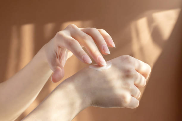 istock Application of cream, lotion on hands. Beautiful female hands rub moisturizing liquid into delicate skin, in rays of sunlight on brown background. Concept of care and beauty 1372080148
