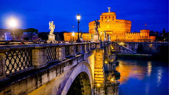 Rome, Italy, February 19 -- A suggestive and idyllic evening view of Ponte Sant'Angelo and Castel Sant'Angelo, in the historic heart of Rome. This bridge was built over the River Tiber at the behest of the emperor Hadrian in 134 AD to connect the heart of the Ancient Rome with his mausoleum, currently Castel Sant'Angelo. A few centuries later, under the pontificate of Pope Clement IX, the architect and sculptor Giovanni Lorenzo Bernini was commissioned to create the current balustrade decorated with ten statues of the Angels of the Passion of Christ. According to the Christian tradition, each Angel holds one of the relics of the Passion of Christ, such as the cross, the veil of Veronica, the nails, the spear, the pillar of the scourging, etc. Designed by Bernini, the statues were made under his direction in 1669 by the pupils present in his school of sculpture. Built around 123 AD as a sepulcher for Emperor Hadrian and his family, Castel Sant'Angelo has been used over the centuries as a fortress, prison and refuge by the Popes due to its proximity to the Vatican. It is currently owned by the Italian State and is used for visits and cultural events. In 1980 the historic center of Rome was declared a World Heritage Site by Unesco. Super wide angle image in 16:9 and high definition format.