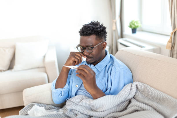 istock Sickness, seasonal virus problem concept. Man being sick having flu lying on bed looking at temperature on thermometer. Sick man lying in bed with high fever. Cold flu coronavirus, covid19 1372081101