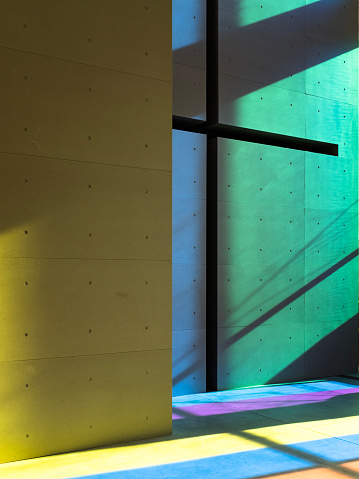 The midday sun shines on the multi-colored glass to create multi-colored rays that hit a concrete façade