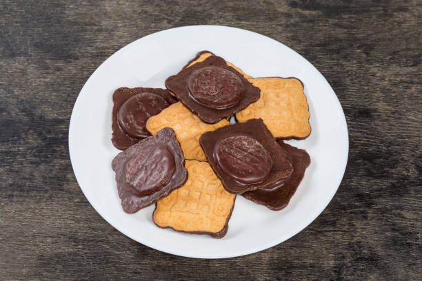 Cookies square shape with chocolate coating on one side and jam filling on a white dish on a black surface