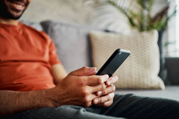 Cropped shot of an unrecognisable man sitting alone in his living room at home and using his cellphone I've always been a gamer at heart scrolling stock pictures, royalty-free photos & images