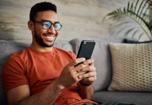 Shot of a young man sitting alone in his living room at home and using his cellphone stock photo