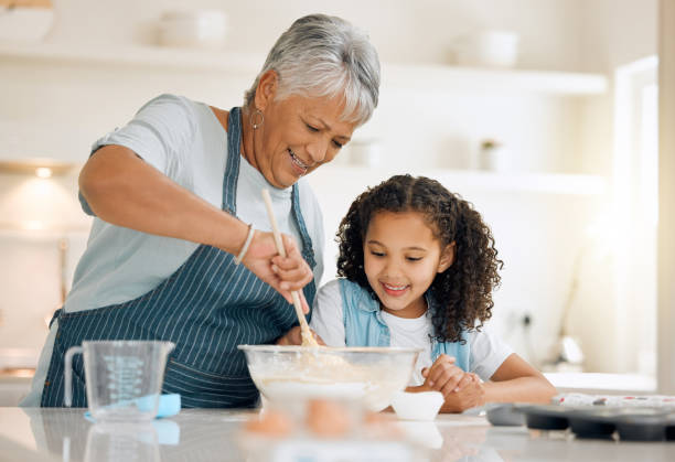 shot of a little girl baking with her grandmother at home - grandmother cooking baking family imagens e fotografias de stock