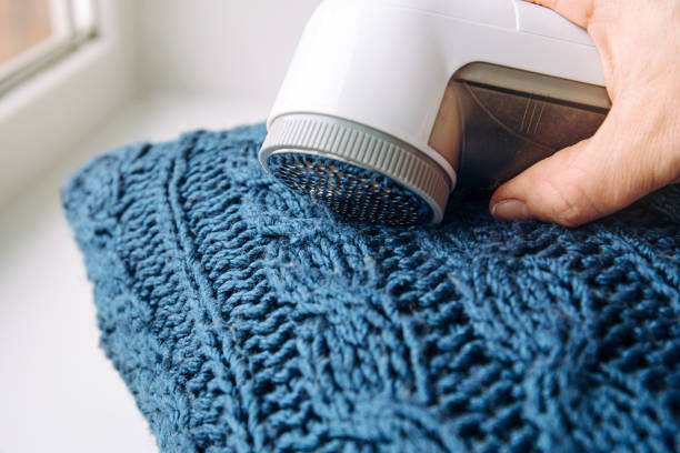 Removing shaving lint fuzz from blue woolen coat sweater, wool clothes maintain concept.