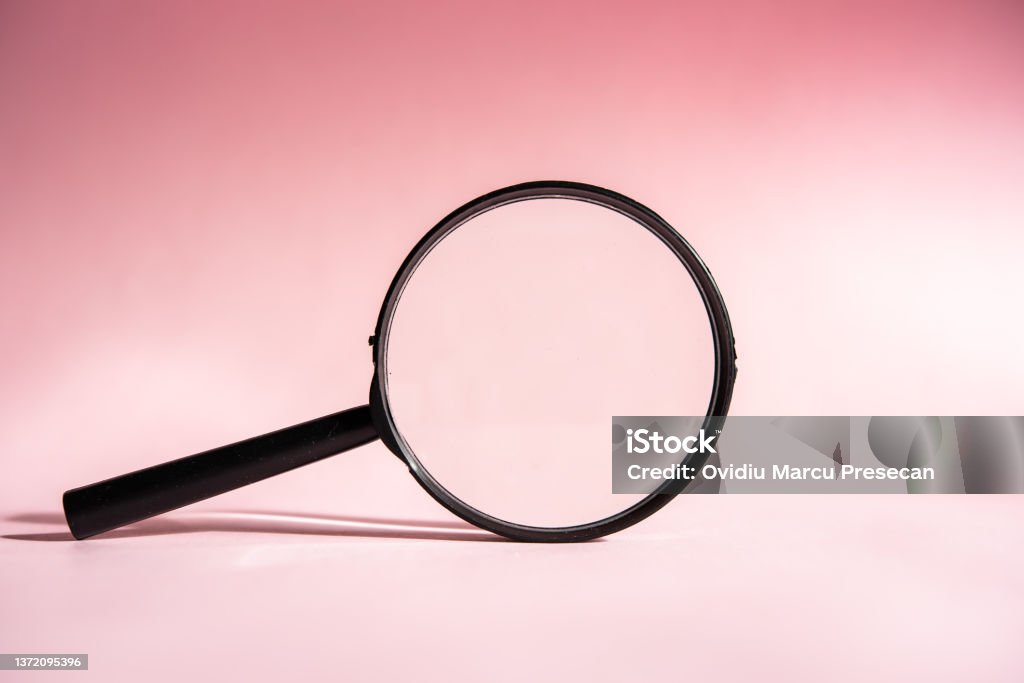 A black magnifying glass on a pink background, concept of search, research, looking for something. Zoom In Stock Photo