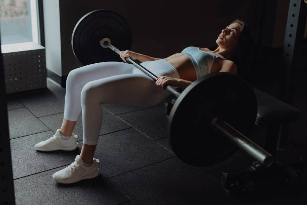 Woman doing buttocks bridge exercise in gym Woman doing buttocks bridge exercise with bar in gym buttocks stock pictures, royalty-free photos & images