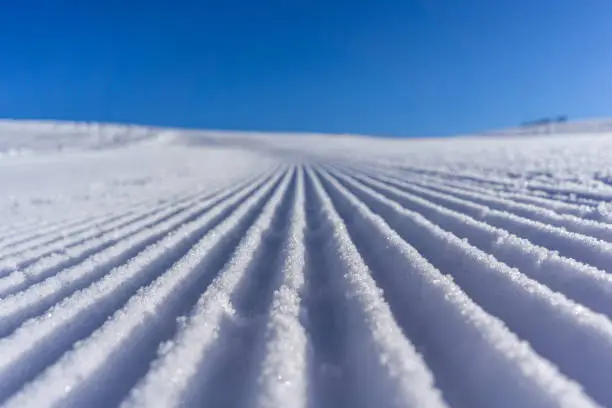 lines in the snow with sun and shadows and blue sky, prepared slope for wintersport and ski