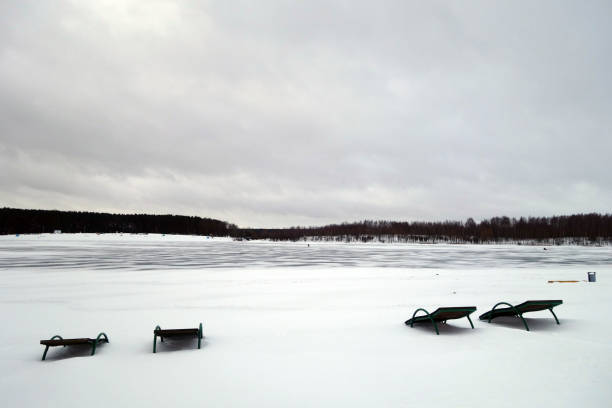 Deck chairs in snow and frozen lake. Seasonal background and scene