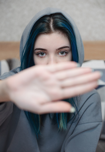 A teenage girl with blue hair covers her face with her hand. Teenage protest. Depression.