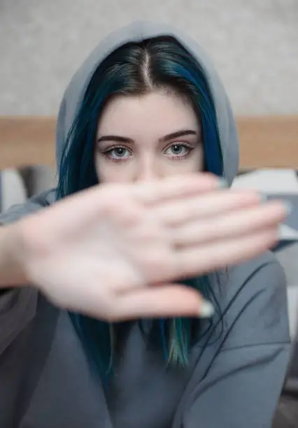 Photo of A teenage girl with blue hair covers her face with her hand