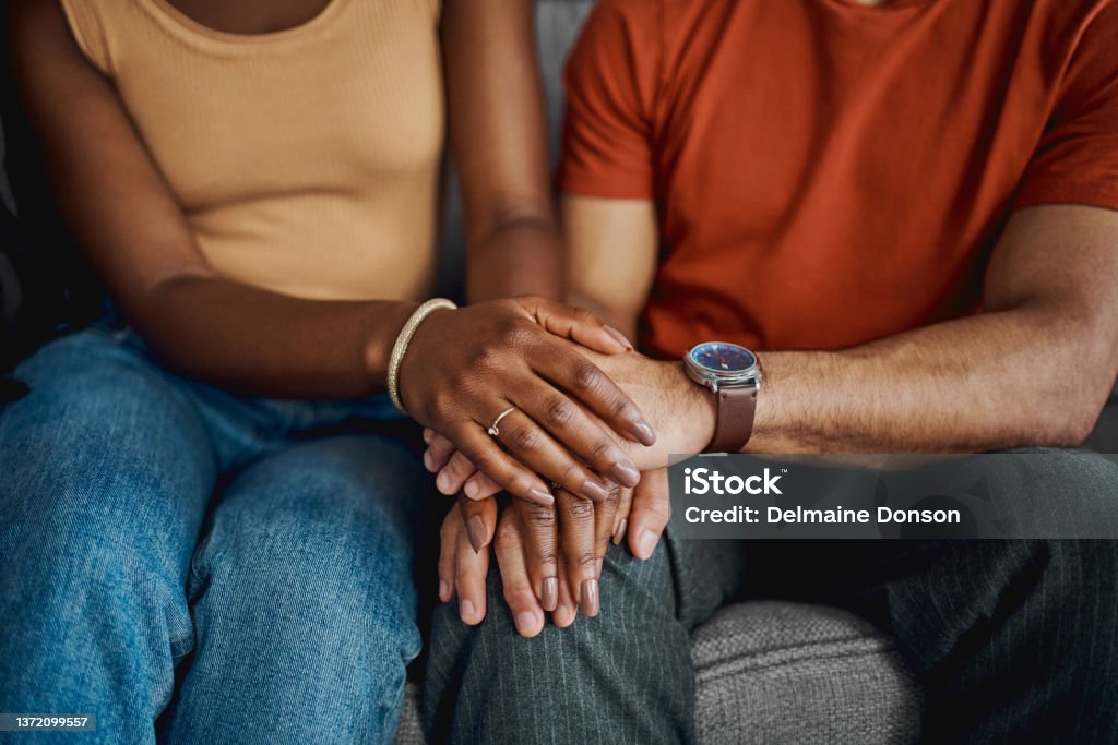 Cropped shot of an unrecognisable couple sitting together on the sofa at home and holding hands You never have to go through anything alone Couple - Relationship Stock Photo