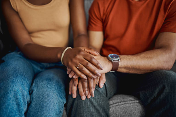 Cropped shot of an unrecognisable couple sitting together on the sofa at home and holding hands stock photo