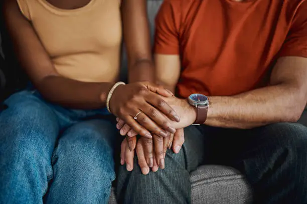 Photo of Cropped shot of an unrecognisable couple sitting together on the sofa at home and holding hands