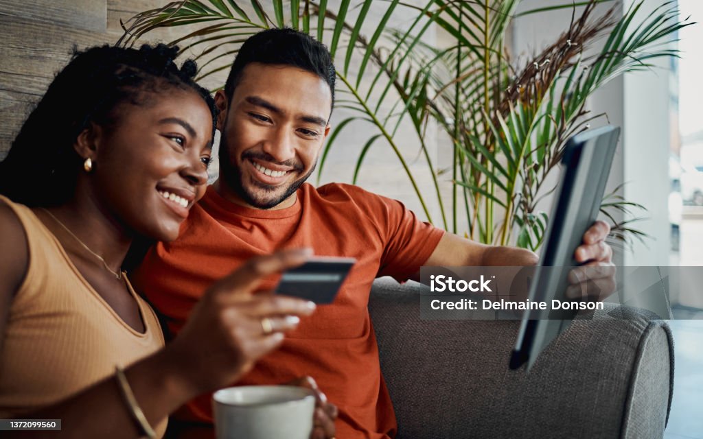 Shot of a young couple sitting together in the living room and using a digital tablet for online shopping We're investing together and in each other Credit Card Stock Photo