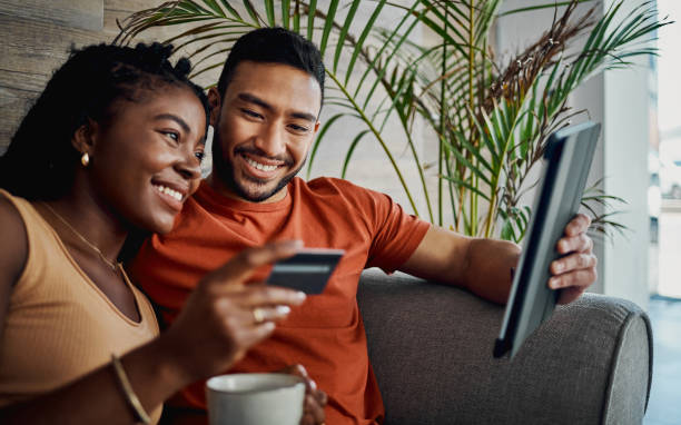 shot of a young couple sitting together in the living room and using a digital tablet for online shopping - electronic banking imagens e fotografias de stock