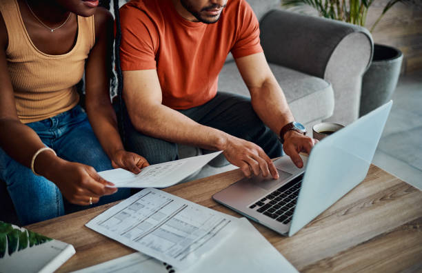 tiro cortado de um casal irreconhecível sentado na sala de estar e usando um laptop para calcular suas finanças - dívida - fotografias e filmes do acervo