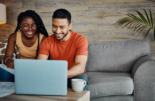 foto de una joven pareja sentada en la sala de estar de su casa y usando una computadora portátil para calcular sus finanzas - home finances couple computer african ethnicity fotografías e imágenes de stock