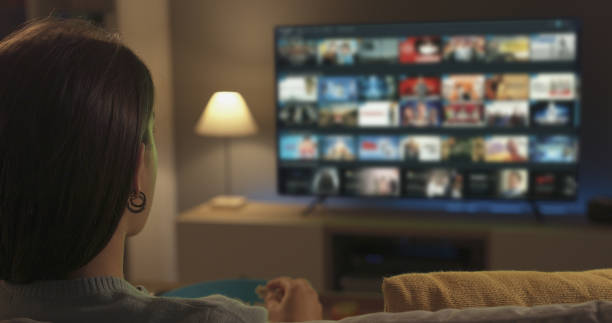 mujer joven viendo video a pedido en su televisor - watching fotografías e imágenes de stock