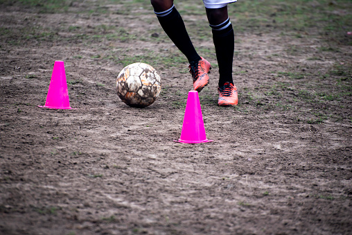 Footballer dribbling ball during training between cones. Young soccer players practicing dribbling.