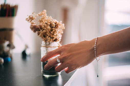 Diamond ring on the women's hand holding a dried flowers on glass pot.