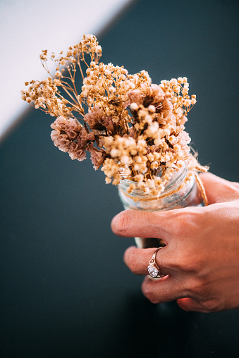 Diamond ring on the women's hand holding a dried flowers on glass pot.