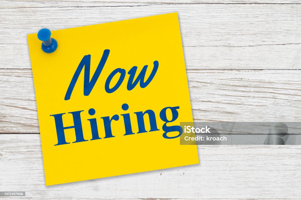 Now Hiring message on a yellow sticky note paper with pushpin Now Hiring message on a yellow sticky note paper with pushpin on weathered wood Job Listing Stock Photo
