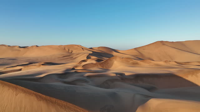 Camera moves toward horizon of giant red desert dunes and blue sky