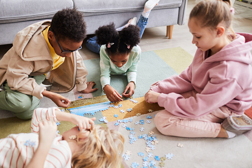 High angle portrait of diverse group of children playing with puzzle game on floor together