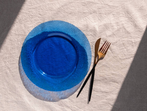 Table setting empty blue glass plate with fork knife on linen cloth top view daylight harsh shadows. Festive dish place. Table setting empty blue glass plate with fork knife on linen cloth top view in daylight harsh shadows. Festive dish place Natural cottagecore styled tableware minimal home decor Countryside aesthetic cottagecore stock pictures, royalty-free photos & images