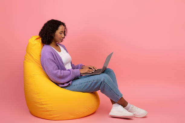 istock Black woman using laptop, sitting in bean bag chair, searching web, working or studying online, checking new site 1372113722