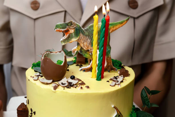 istock yellow cake decorated with three lit multi-colored candles, a chocolate egg and a dinosaur figurine 1372113770
